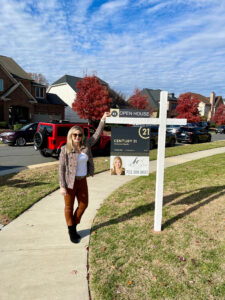 Kelly Ettrich, professional real estate agent in Loudoun County, smiling next to a 'For Sale' sign outside a beautiful property. 